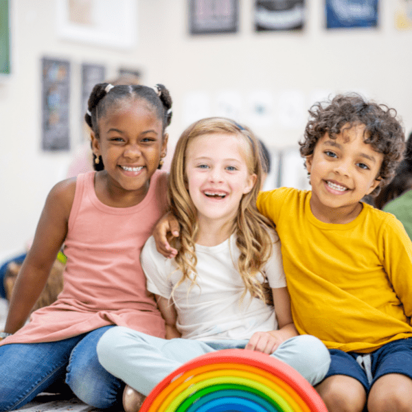 drie vrolijke jonge kinderen op een rij met een regenboog ervoor.